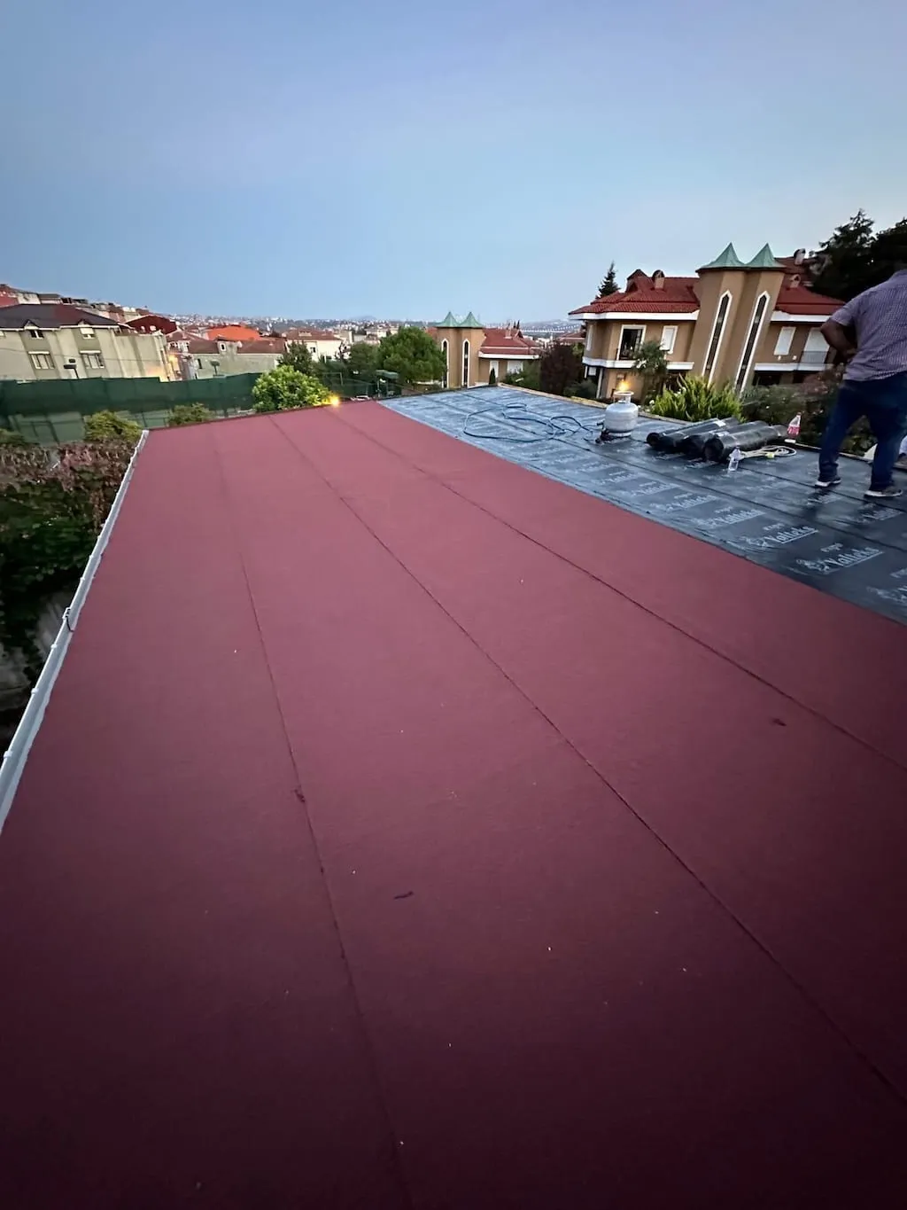 Teras çatıda bordo bitümlü membranın şalomayla eritilerek serildiği, yarısı tamamlanmış su yalıtımı uygulaması
