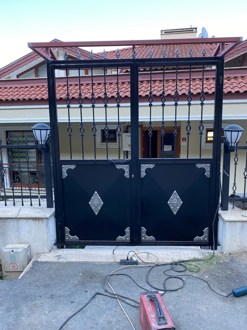 Ferforje bahçe kapısının iki yanında aynı desenle devam eden duvar üstü demir korkuluk panelleri