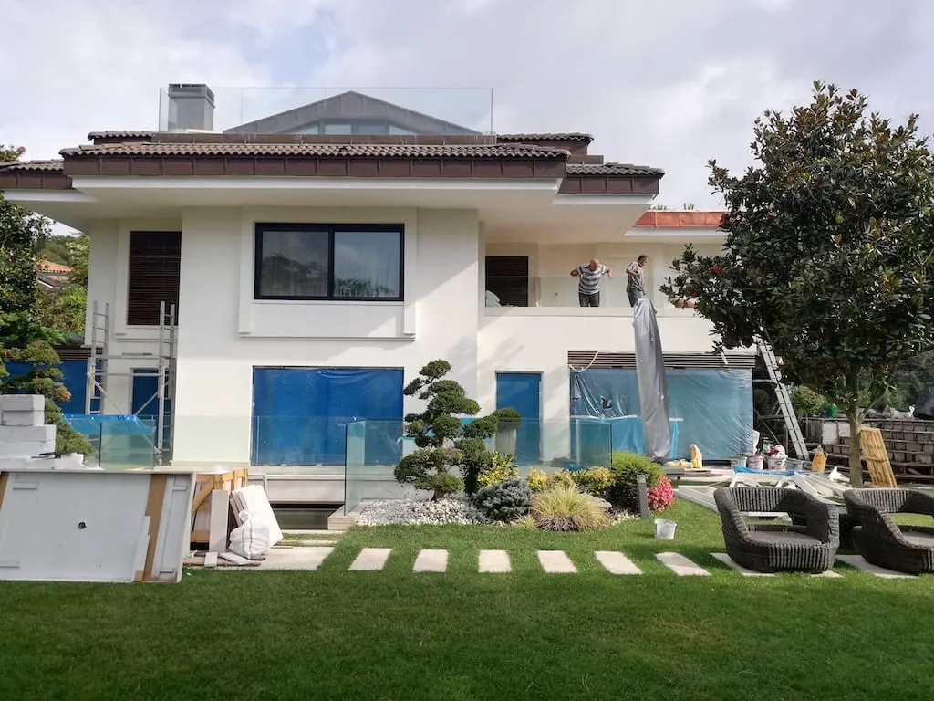 Sarıyer’de dış cephe yenilemesi süren villa: balkonda çalışan iki usta ve koruyucu örtüyle kapatılmış açıklıklar